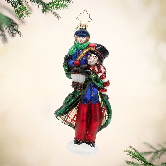 A Cratchit Christmas. Ornament of Tiny Tim on his fathers shoulders while both wear colors of red, green, and blue coats. View of front