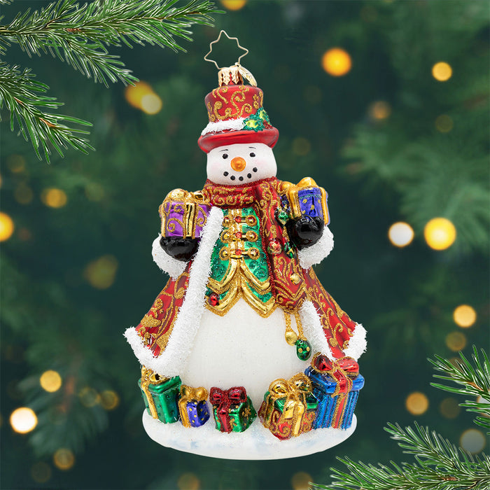 The Jingle Gent. A snowman ornament dressed in a red and gold robe  with a matching top hat, surrounded by and holding presents. View of front.