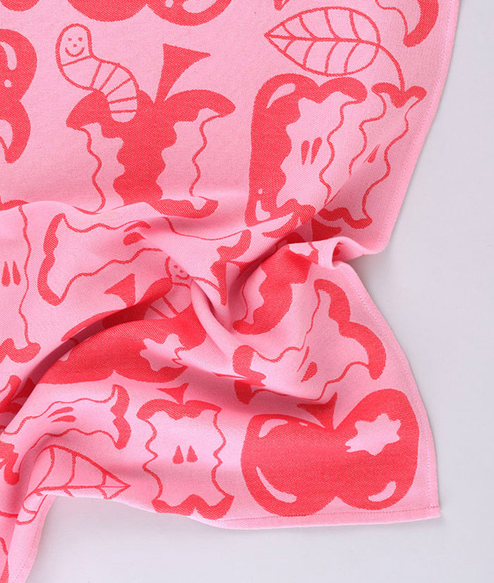 Corner detail of the pink apple a day tea towel featuring half eaten apples and  cartoon worms
