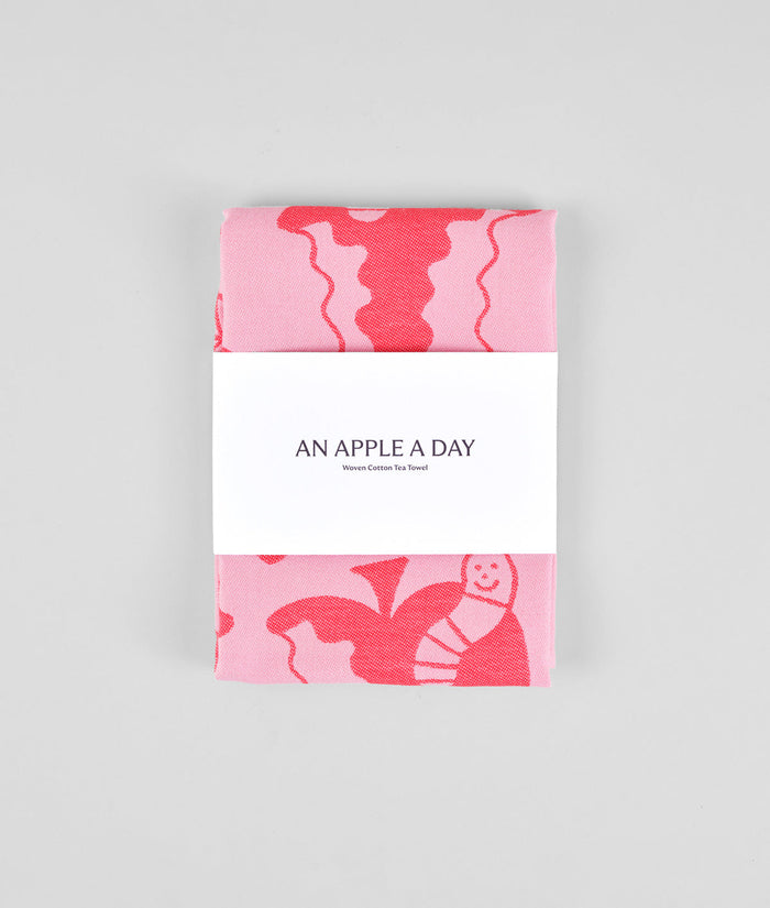 packaging detail of the pink apple a day tea towel featuring half eaten apples and  cartoon worms