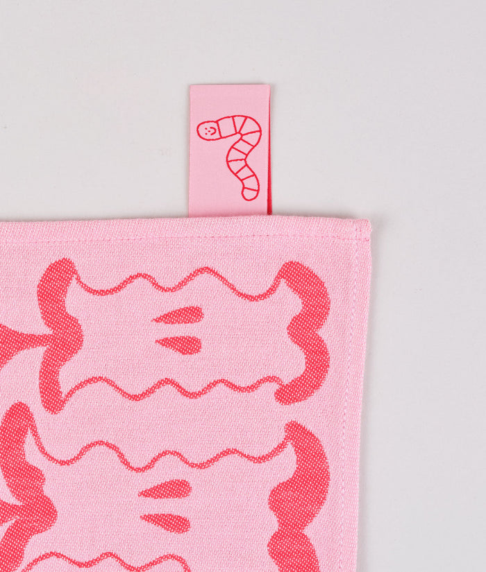 label detail of the pink apple a day tea towel. the pink label is a cartoon worm