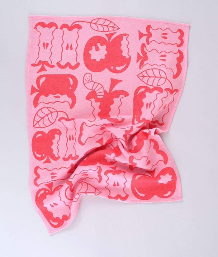 Full view of the pink apple a day tea towel featuring half eaten apples and cartoon worms