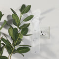 White wall socket with a white remote control next to green leaves on a light gray background