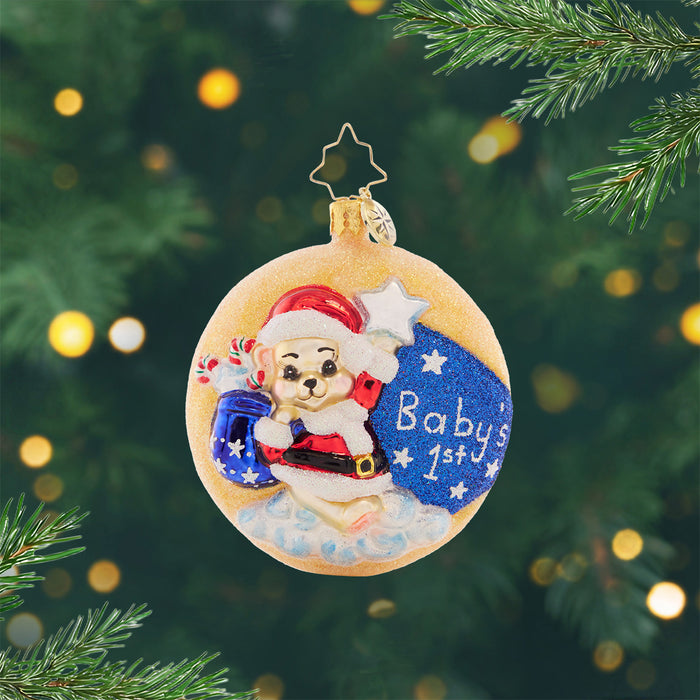 Darling 1st Christmas Gem. Round ornament of a bear in a red Santa suit, holding a starry blue gift bad, on top of a glittery moon. View of front