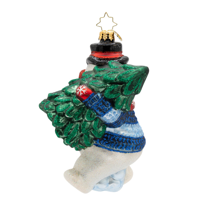 Back view of a decorative Christmas ornament shaped like a snowman holding a small tree, wearing a blue sweater and red mittens.