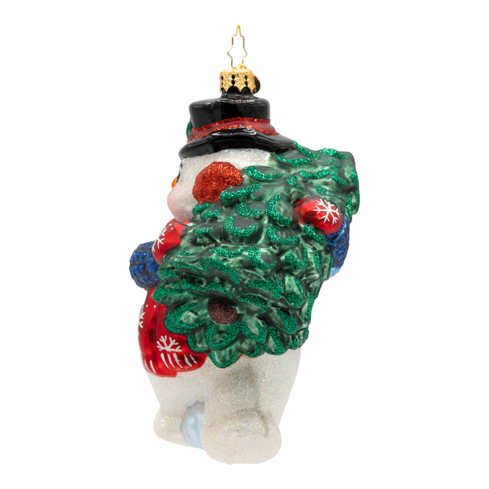 Side view of a decorative Christmas ornament shaped like a snowman holding a small tree, wearing a blue sweater and red mittens.