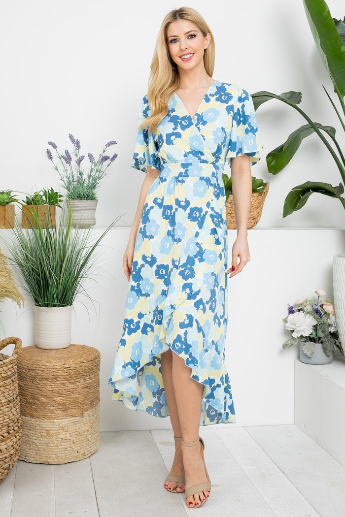 Woman wearing a blue floral dress standing in a room with plants.