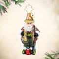 Fly Fisher Claus Gem. Ornament of Santa dressed in a green and brown fishing outfit with a red bucket and brown fishing pole. View of front