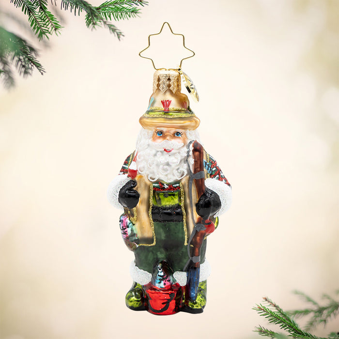 Fly Fisher Claus Gem. Ornament of Santa dressed in a green and brown fishing outfit with a red bucket and brown fishing pole. View of front