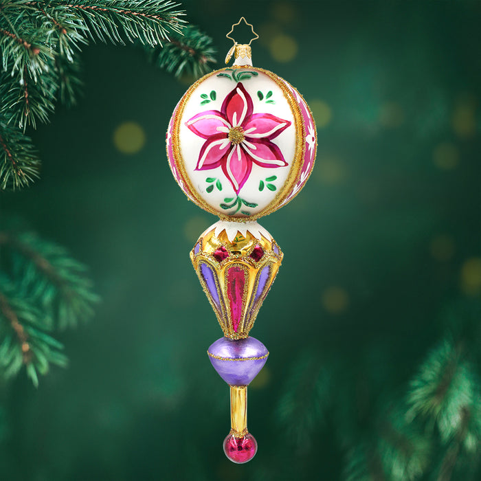 This ornament features a white sphere decorated with a vibrant pink flower. Below is multifaced jewel like section that changed between pink and purple with gold trim. View of front