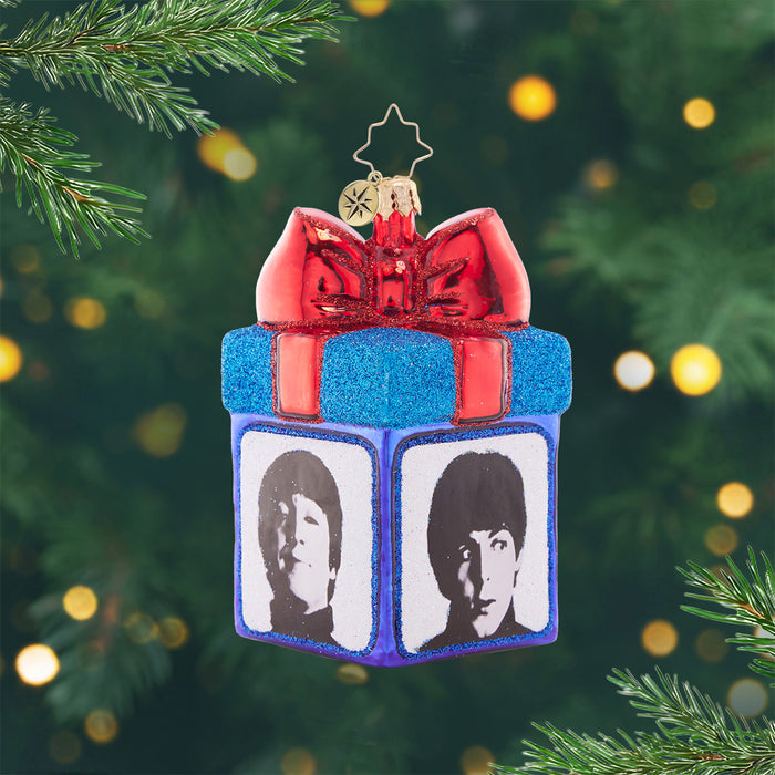 Gather Round for Gifting. Ornament in the shape of a present colored in blue with a big red bow at the top, and a different Beatle member on each side. View of front