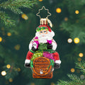 I Believe in Wine Santa Gem. Ornament of Santa in a white sweater with stripes and a green apron sitting on a brown barrel and hold a pink bottle and glass of wine. View of front
