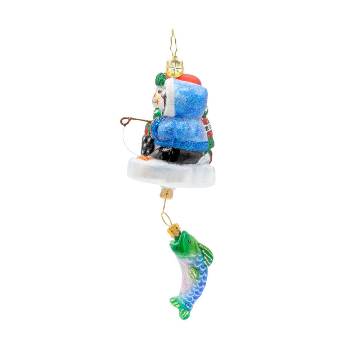 Ice Fishing Snow Pals Gem ornament. A snowman and penguin sit bundled up on a block of ice with a fishing pole. A fish dangles below. View of right side.