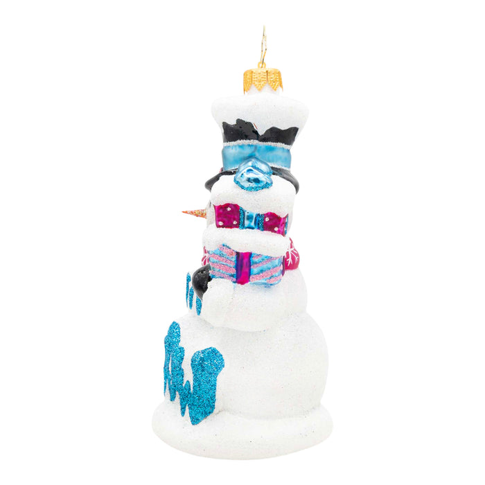 Side of a decorative snowman ornament holding two presents in the colors pink and blue in one had and in the other a broom, with the phrase "Let It Snow" in blue on the front.