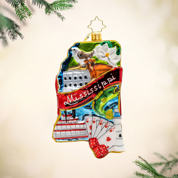 Ornament shaped as the state of Mississippi and featuring a deck of cards, cruise, fish, bird, as well as a red banner with Mississippi. View of front