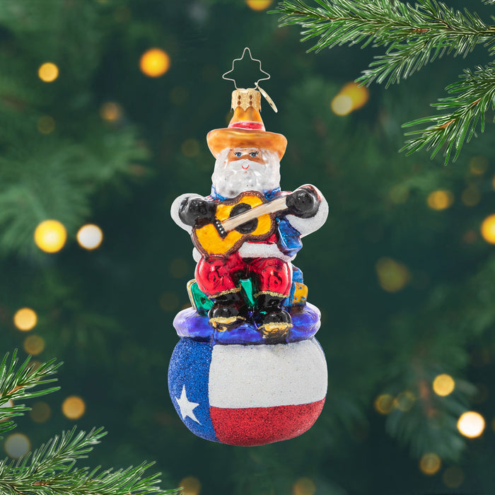 Pride of Texas Santa. Ornament of Santa playing a guitar on top of a gift bag with the Texas flag. View of front