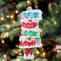 Decorative Christmas ornament with names on bookshelves against a blurred Christmas tree background