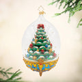Royal Elegance Spruce. Ornament of a bright green spruce tree decked in gold ribbon and gems of gold, red, and blue, while inside a dome with a blue and gold base.