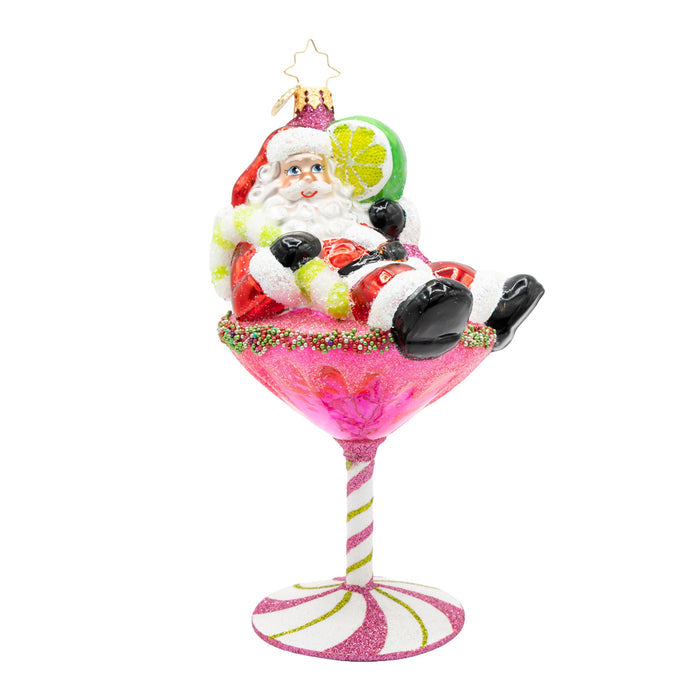Front view of ornament of Santa laying on top of a pink martini drink with a base of a pink peppermint, while holding a lime.