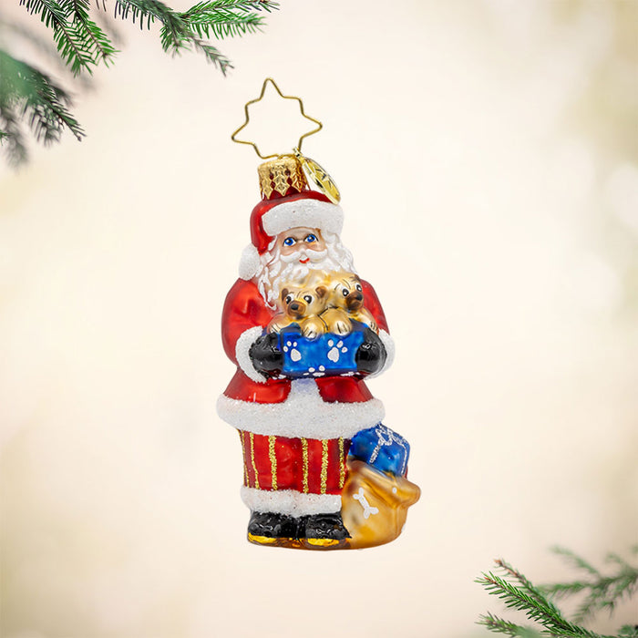 Santa's Pug-palooza Gem ornament. Santa holds a box of pug puppies. There is a gift sack of presents by his feet. View of front.