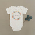 She's Here Wildflower Floral Wreath Organic Baby Onesie®
