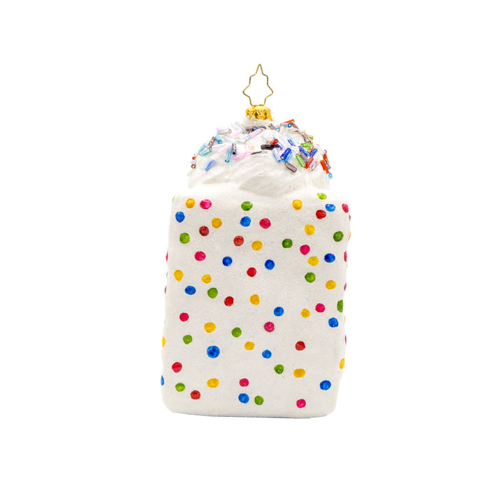 Slice of Joy ornament. A tall slice of rainbow layered cake with sprinkles and fruit on top. View of left side.
