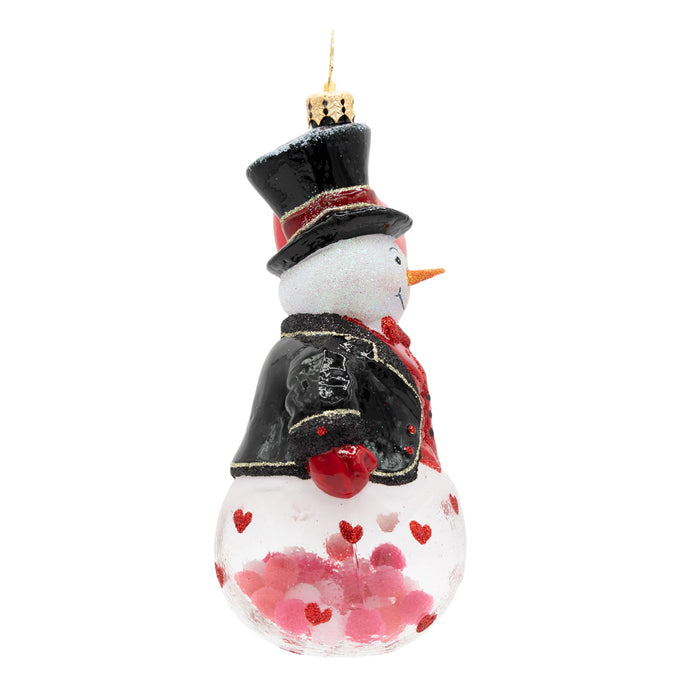 Side view of a snowman ornament with a top hat, black coat, and red heart design on the base of the ornament on a white background
