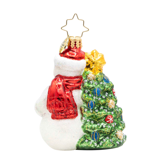 Back of snowman ornament wearing a red and white trimmed santa hat and red scarf next to a decorated tree on a white background