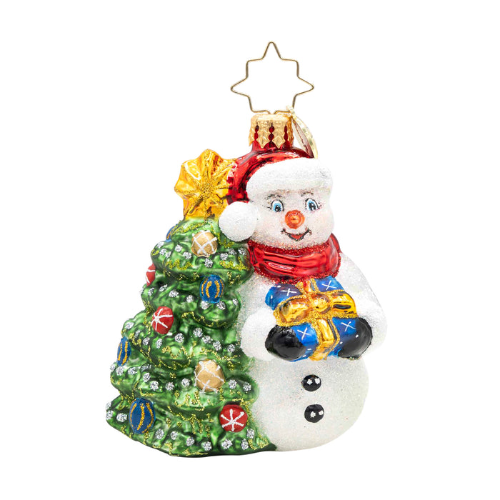 Snowy & Bright! Gem. Snowman ornament dressed in a red hat and scarf, holding a blue present next to a decorated Christmas tree. View of front