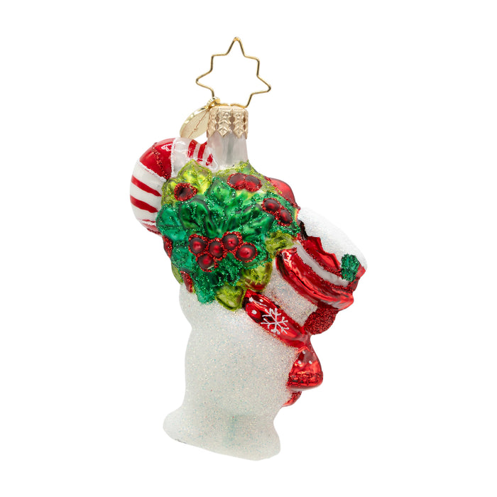 Back of a snowman ornament with a green wreath attached. details of a red and white striped hat and the red scarf, with snowflake patterns are seen from the back angle of ornament. corner of the candy cane peaks out of top left corner of the ornament .