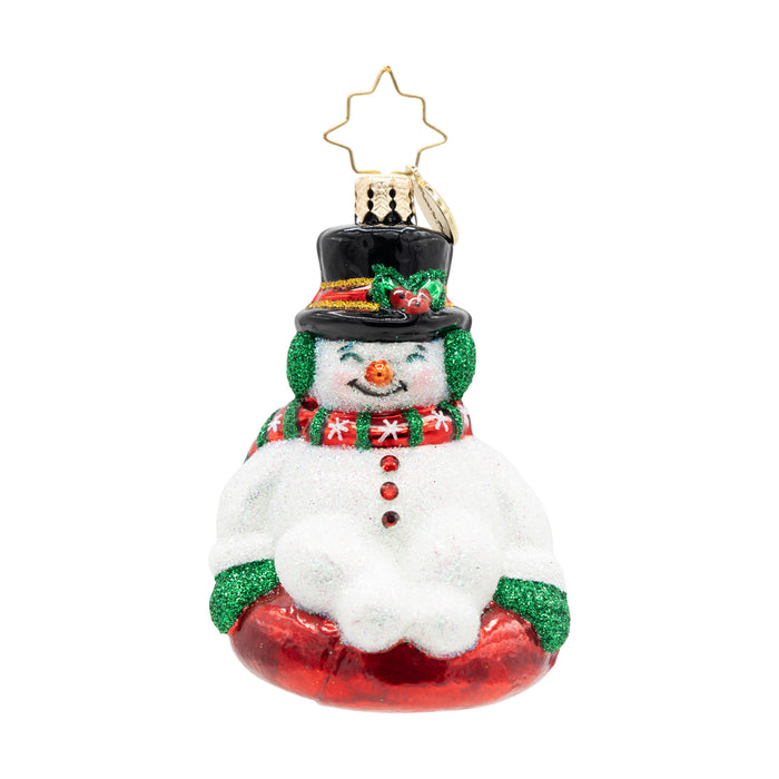 Front view of a snowman ornament wearing a red and green scarf on a red sled.