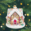Sweet Treat House.  A gingerbread house ornament with a white snowy roof and colorful gems and five golden windows in the front and to decorated Christmas trees. View of front