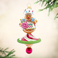 Sweet Winter Whirl. Ornament of a gingerbread man wearing a white hat and apron with gems while holding a jar of cookies with a base in the shape of a spinner in pink, white, and green stripes. View of front