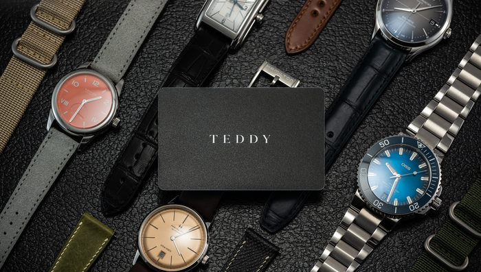Teddy gift card placed among a collection of watches and straps on a textured surface