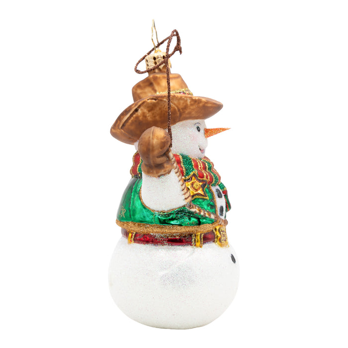 Side view of a snowman ornament with cowboy hat, red, gold and green striped scarf, and lasso. Green vest with gold badge detail. Red and gold buckled belt. Placed on a white background.