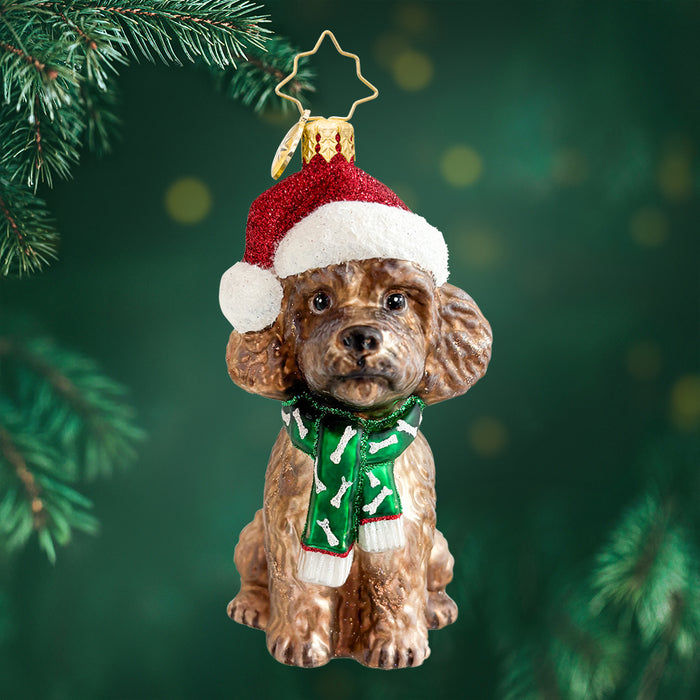 Ornament of a brown doodle wearing a Santa hat and a green scarf with bones. View of front