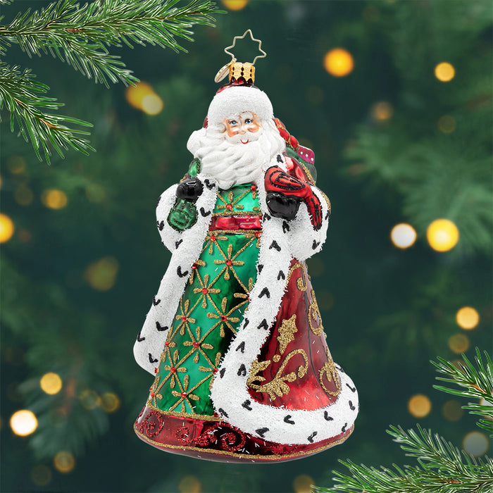 The Royal Yuletide Giver. A Santa ornament with him dressed in a green, red, and gold robe while holding a cardinal and a green bag of presents. View of front.