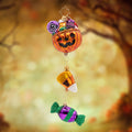 Trick or Treat Trio. This ornament consist of a bright orange pumpkin holding candy corn which is holding a purple candy. View of front