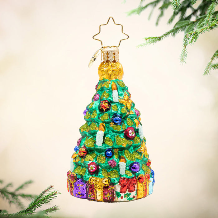Twinkling Tree Gem. Ornament of a sparkly Christmas tree decorated in red, blue and purple ornaments with gold details and a base full of colorful presents. View of front