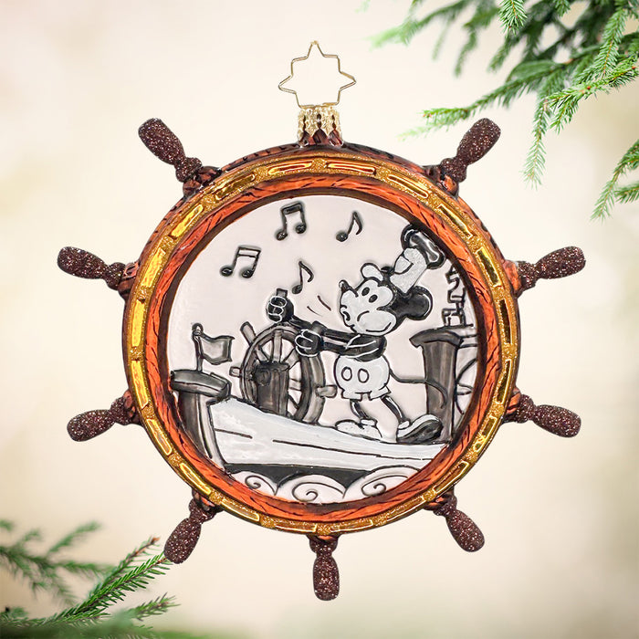 This ornament is shaped in ships wheel in a warm brown color with gold accents. It features the classic black and white Micky Mouse whistling and steering a boat. View of front