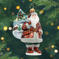 Woodland Noel. Santa ornament of him in a red suit with gold leaf patterns and holding a bag painted with a log cabin scene along with a tree inside the bag. View of front
